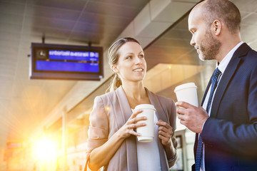 Portrait of businessman and businesswoman holding cup of coffee while talking and waiting for the train