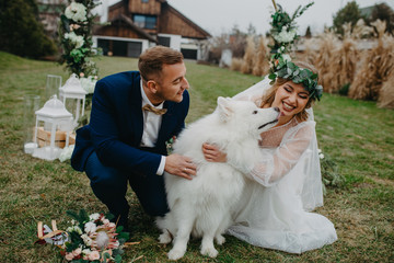 Newlyweds play with dog on background of lawn and house.