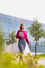 Portrait of young attractive businesswoman walking while holding digital tablet