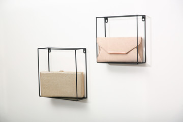 Metal shelves with stylish woman's bags on white wall