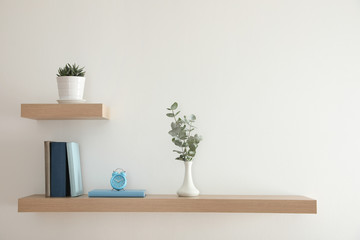 Wooden shelves with beautiful plants, alarm clock and books on light wall - Powered by Adobe