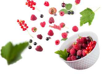 Fresh berries mix with green leaves flying and falling down into a bowl on white background