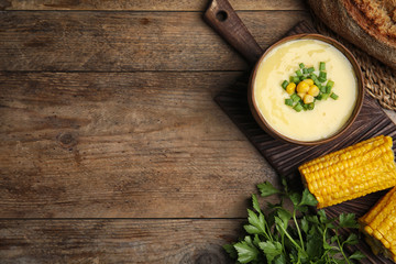 Delicious corn cream soup served on wooden table, flat lay. Space for text