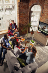 Excited group of people watching american football, sport match at home. Multiethnic group of emotional friend, fans cheering for favourite national team, drinking beer. Concept of emotions, support.