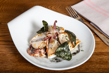 Grilled squid dish with sauteed black sausage, candied onion and crispy nori seaweed on wooden table. Grastronomy