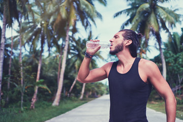 Sport lifestyle. Handsome strong young man drinking water outdoors.