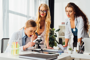 selective focus of sexy nurse looking through microscope near women
