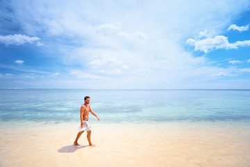 Fototapeta na wymiar Tropical vacation. Young man walking by beautiful white sand sea beach.