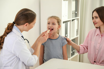Obraz premium Mother and daughter visiting pediatrician. Doctor examining little patient's throat in hospital