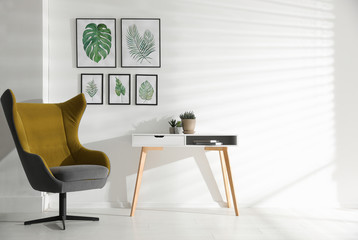Stylish room interior with comfortable armchair and paintings of tropical leaves