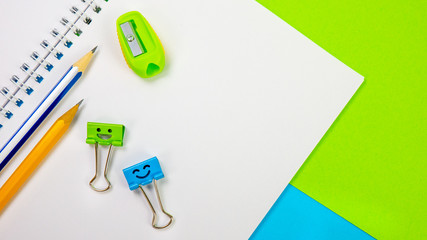 School Notepad with Yellow and Blue Pencil and Smile Binder Clip, Pencil Sharpener on Blue Green Background. Spiral notebook on table. Business, office supplies or education concept