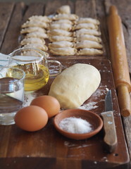 Wooden background with dumplings and dough ingredients for making dumplings. Food and cooking utensils on a brown kitchen board. Place for text. The concept of cooking dough.
