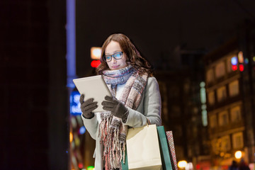 Fototapeta na wymiar Portrait of young attractive woman smiling and using digital tablet while on night shopping