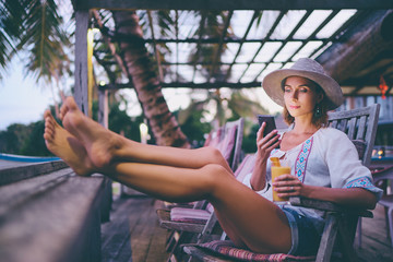 Vacation and technology. Young pretty woman in hat using smartphone sitting at beach cafe bar.