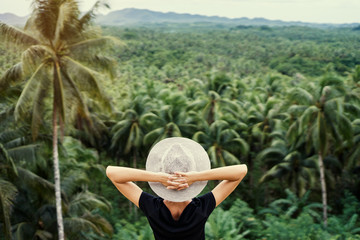 Fototapeta premium Tropical vacation. Young woman in hat enjoying the view of beautiful coconut palms plantation.