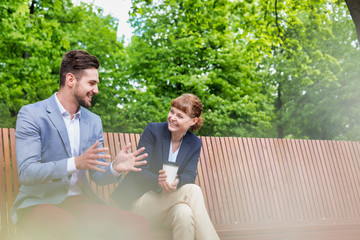 Portrait of handsome businessman gesturing and talking to businesswoman while sitting on bench during office break