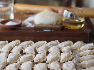 Wooden background with dumplings and dough ingredients for making dumplings. Food and cooking utensils on a brown kitchen board. Place for text. The concept of cooking dough.