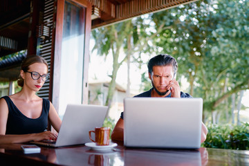 Fototapeta premium Coworking and freelance concept. Young bearded man and young woman working together on laptop computers while sitting on cafe terrace.