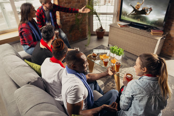 Excited group of people watching american football, sport match at home. Multiethnic group of emotional friend, fans cheering for favourite national team, drinking beer. Concept of emotions, support.
