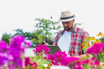 Portrait of mature gardener writing report on clipboard over flowers in shop