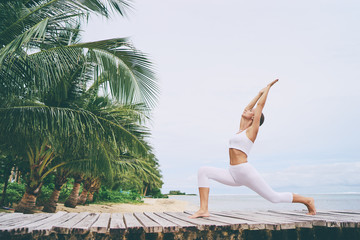 Gelukkig jonge vrouw permanent in yoga pose op houten pier. Yoga beoefenen met ocean beach op de achtergrond.