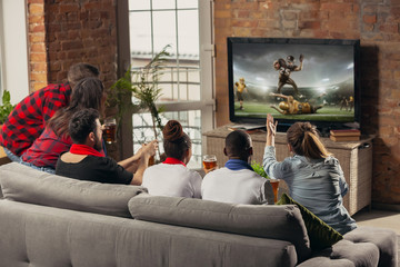 Excited group of people watching american football, sport match at home. Multiethnic group of emotional friend, fans cheering for favourite national team, drinking beer. Concept of emotions, support.