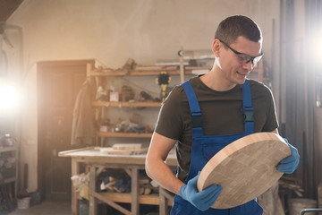 Professional carpenter with round piece of wood in workshop