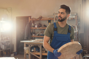 Professional carpenter with round piece of wood in workshop