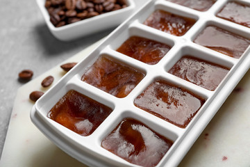 Ice cubes in tray and coffee beans on grey table, closeup