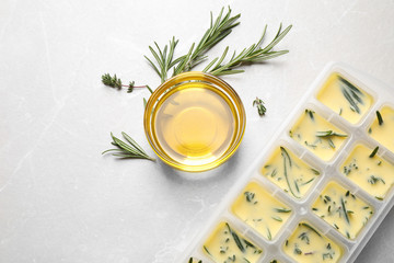 Ice cube tray with herbs frozen in oil and fresh rosemary on grey table, flat lay © New Africa