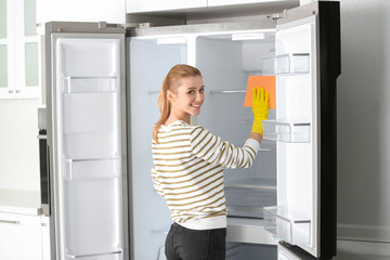Woman in rubber gloves cleaning empty refrigerator at home