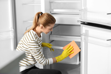 Woman in rubber gloves cleaning empty refrigerator with rag at home