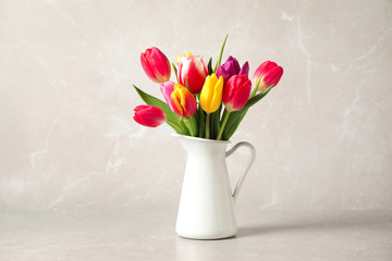 Beautiful spring tulips in vase on table against light marble background