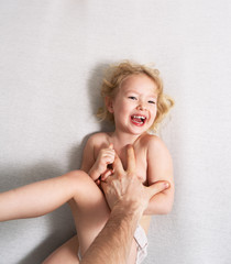 Family time: a little girl lies on the bed and laughs cheerfully because of the tickling of her...