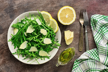 Light diet salad of arugula, parmesan and lemon on a dark rustic background. Top view, flat lay, copy space.