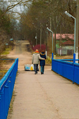 A young man and a girl walk embracing along the bridge over the river on a cool autumn day