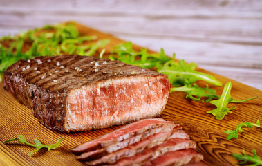 Medium rare beef sirloin with arugula on cut board.