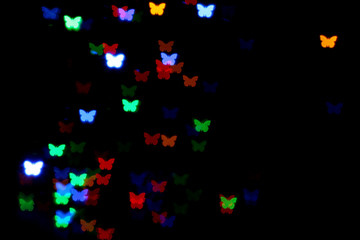 Blurred view of butterfly shaped lights on black background. Bokeh effect