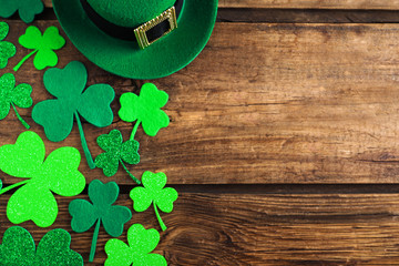 Green leprechaun hat and clover leaves on wooden table, flat lay with space for text. St. Patrick's...