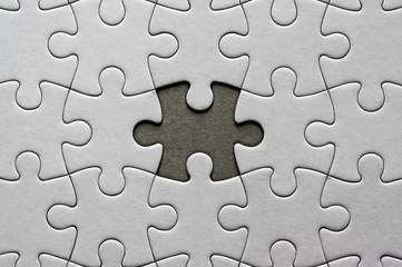 Blank, white jigsaw puzzle close up. One piece is missing