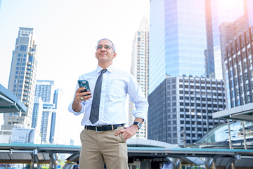 Fototapeta premium Successful businessman standing outdoors smiling and holding phone in his hands in the background.