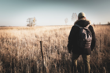 Male traveler with a backpack walking towards the horizon on a wild meadow, Nowiny, Poland