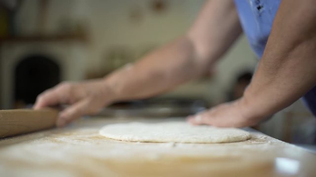 Woman chef baker making a pizza shaping a dough on a wooden board with a rolling pin in a restaurant pizzeria or in the kitchen of a house. Food concept.