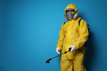 Man wearing protective suit with insecticide sprayer on blue background, space for text. Pest...