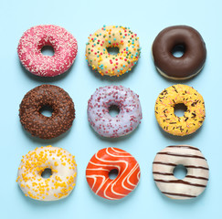 Delicious glazed donuts on light blue background, flat lay