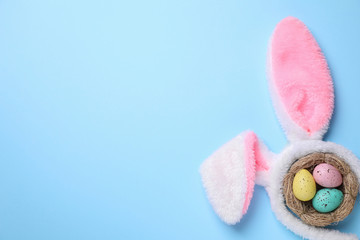 Headband with bunny ears, painted eggs and space for text on light blue background, flat lay. Easter holiday