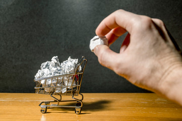 a hand throws crumpled paper into a miniature grocery cart