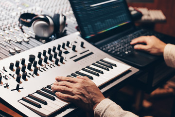 music producer hands composing a song on synthesizer keyboard and laptop computer in recording...
