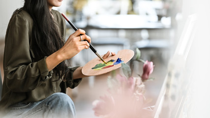 Cropped image of young beautiful artist girl sitting in front the drawing canvas while painting an oil color at the modern studio. Beautiful artist and gallery studio concept. - obrazy, fototapety, plakaty