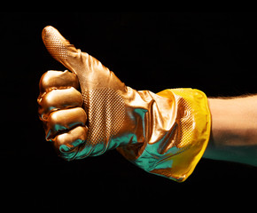 Image of gold painted Like gesture of hand in yellow rubber glove on black background